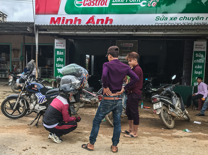 =We stopped briefly at a bike shop in a tiny town. Sherlock added oil and removed a screw from his rear tire. This is very typical of stores/businesses: front wide open, guys hanging out, and work conducted out front or just inside the storefront.