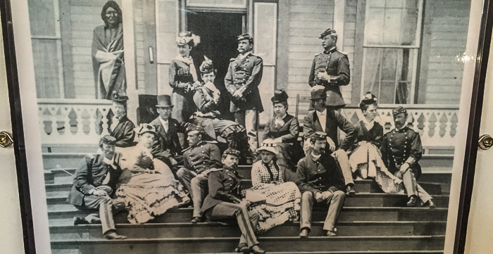 A photo of Myles Keogh at the Custer home in 1875. Keogh is in the center holding a fan, Tom Custer is far left, and George Custer far right. The original photo is from the North Dakota Historical Society.