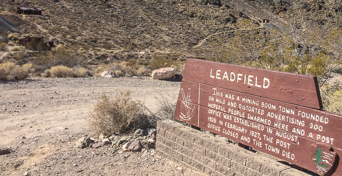 The Leadfield ghost town sign with a few old buildings in the distance.