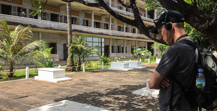 Chris in the center courtyard at Tuol Sleng, listening to the audio guide. He stands in front of 14 white graves, for the 14 unidentified victims left behind when the Khmer Rouge fled in 1979.